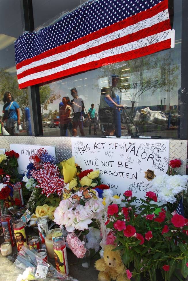 Shoppers are reflected in a window Thursday, June 12, 2014 near a memorial for Joseph Wilcox at the Wal-Mart where he was killed. 