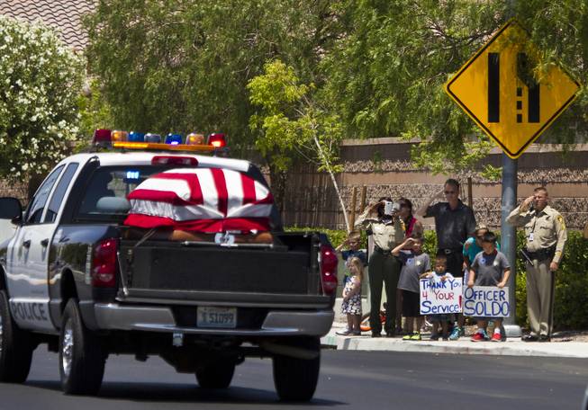 The body of slain Metro Officer Igor Soldo drives past saluting officers and others gathered en route to the Palm Mortuary for funeral services on Thursday, June 12, 2014.