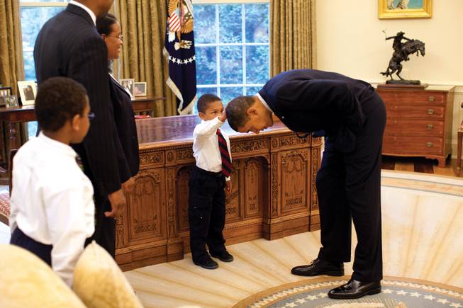 President Barack Obama bends over so the son of a White House staff member can feel his hair during a visit to the Oval Office on May 8, 2009.