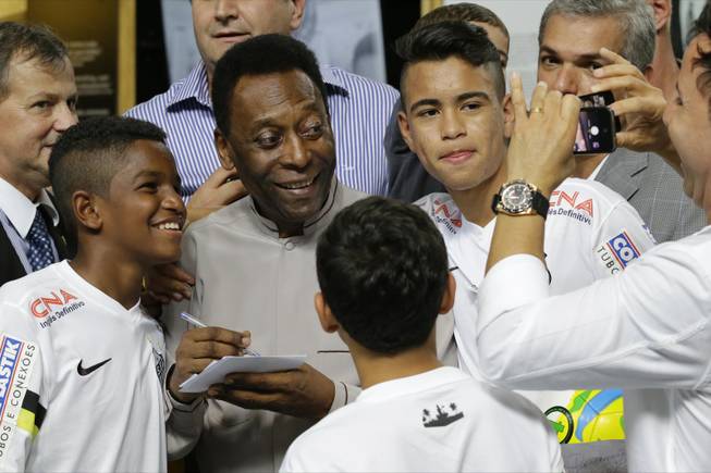 Soccer great Pele pose for a photo next to young players of the Santos soccer team during the inauguration of the Pele Museum in Santos, Brazil, Sunday, June 15, 2014. The Pele Museum exhibits his personal collection, pictures, films, trophies and printed material about his history as a soccer player and personality.