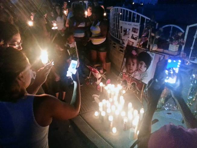 People are shown at a candlelight vigil Thursday, June 19, 2014, at the home where two children died in an early-morning fire.