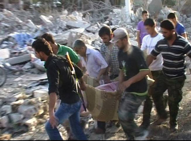 In this photo taken from video released by the Syrian official news agency SANA, Syrians carry a victim from a massive car bomb in the central village of Horrah, in the province of Hama, Syria, Friday, June 20, 2014. A massive car bomb exploded Friday in a government-controlled village in central Syria, dozens of people were killed and wounded, Syrian state media reported.