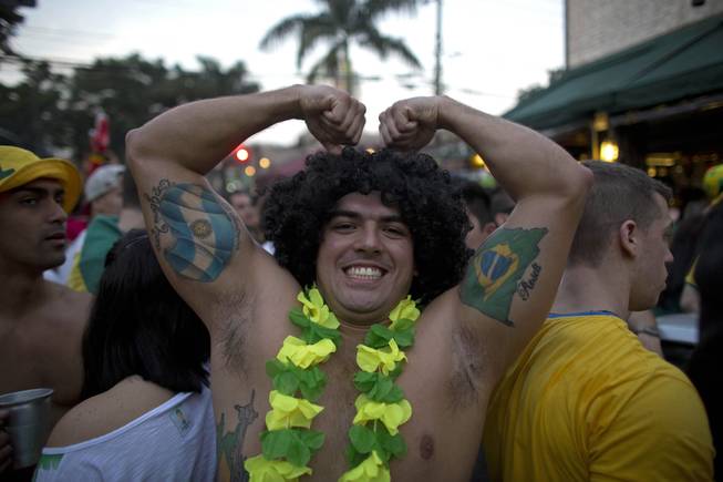 A fan shows off his muscles sporting tattoos of national flags from Brazil and Argentina, as thousands watch the World Cup group A match between Brazil and Cameroon, in the Vila  Madalena neighborhood, in Sao Paulo, Brazil, Monday, June 23, 2014. Brazil won 4-1. (AP Photo/Dario Lopez-Mills)