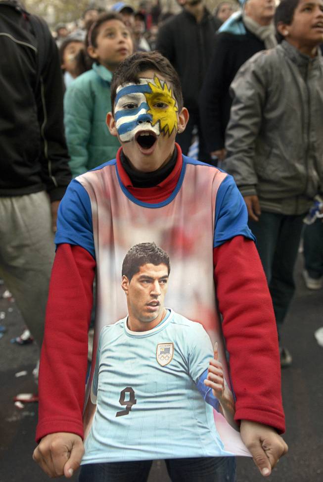 A soccer fan, with his face painted to represent his country's flag and wearing a T-shirt with an image of Uruguayan footballer Luis Suarez, cheers as he watches a live broadcast of the World Cup match between England and Uruguay in downtown Montevideo, Uruguay, Thursday, June 19, 2014. Suarez scored twice to give Uruguay a 2-1 victory over England, making an instant impact on his return from injury to revive his team's Group D campaign. 