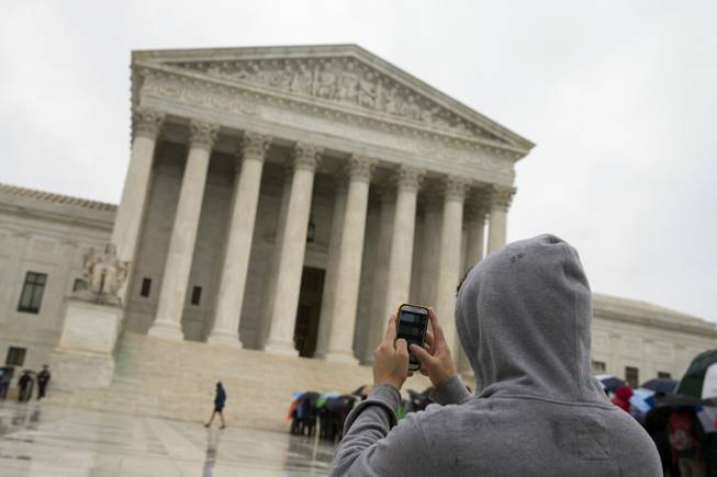 This April 29, 2014, photo shows a Supreme Court visitor using his cellphone to take a photo of the court in Washington. A unanimous Supreme Court ruling says police may not generally search the cellphones of people they arrest without first getting search warrants.