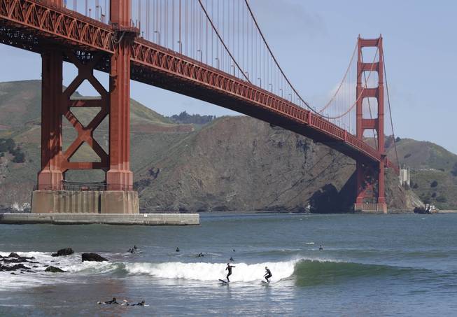 Two surfers ride a wave near Fort Point below the Golden Gate Bridge in this May 3, 2014, file photo in San Francisco.
