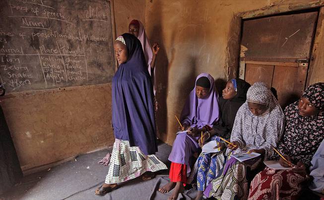 Maimuna Abdullahi, left, moves toward the blackboard during class as she and others attend school in Kaduna, Nigeria, Monday, June 2, 2014. 