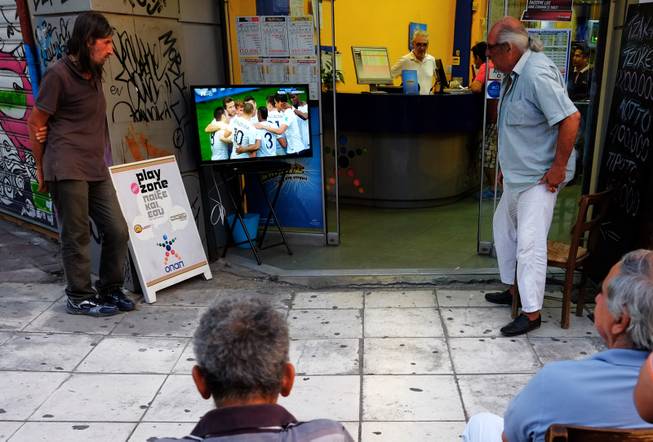 People watch the World Cup round of 16 soccer match between France and Nigeria on TV outside of a betting shop in central Athens, Monday, June 30, 2014. France won the match 2-0, played at the Estadio Nacional stadium in Brasilia, Brazil.  