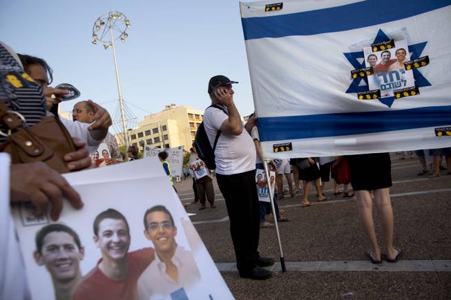 In this Sunday, June 29, 2014, photo, Israelis hold the national flag with photos of the three missing Israeli teens, feared abducted in the West Bank on June 12, during a rally calling for their release, in Tel Aviv, Israel. Security officials said Monday, June 30, 2014, that the Israeli military discovered the bodies of the teens.