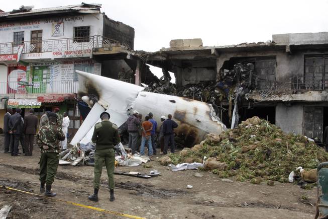 Soldiers and airport staff members look at the wreckage of the Fokker 50 cargo plane after it crashed shortly after takeoff at Kenyatta International Airport, Wednesday, July 2, 2014.