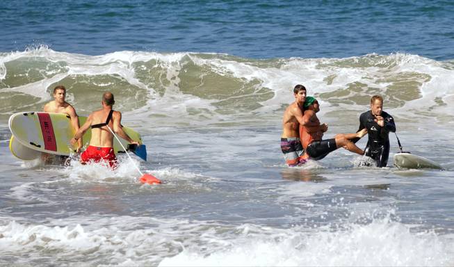 Two men carry a swimmer, second from right, after he was bitten by a great white shark, as lifeguards close in at left in the ocean off Southern California’s Manhattan Beach on Saturday, July 5, 2014. 