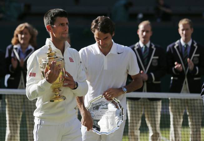 Novak Djokovic of Serbia, left, holds the trophy after defeating Roger Federer of Switzerland in the men's singles final at the Wimbledon All England Lawn Tennis Championships on Sunday, July 6, 2014, in London, England.