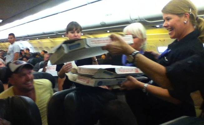 In this photo taken Monday, July 7, 2014, a Frontier Airlines flight attendant passes out pizza to passengers aboard a Denver-bound flight diverted to Cheyenne, Wyo. The airplane pilot treated his passengers to the pizza after they were diverted.