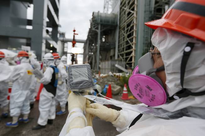 A Tokyo Electric Power Co.'s staff member measures the radiation in the air as workers prepare materials which will be used to create a frozen underground wall to surround the crippled reactor buildings at Tokyo Electric Power Co.'s Fukushima Daiichi Nuclear Power Plant in Okuma, Fukushima Prefecture, northeast of Tokyo, Japan, Wednesday, July 9, 2014. TEPCO plans to build a frozen wall around the buildings of Units 1 to 4 at the tsunami-devastated nuclear power plant to stop radiation-contaminated water from flowing to the sea. TEPCO has been struggling with massive amounts of toxic water as the operator continues to pump water into three reactors to keep them cool. The plant suffered meltdowns at three of its six reactors after a tsunami swept through the facilities in March 2011. 