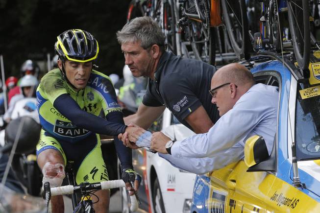 Spain's Alberto Contador gets assistance from his team after crashing during the tenth stage of the Tour de France cycling race over 161.5 kilometers (100.4 miles) with start in Mulhouse and finish in La Planche des Belles Filles, France, Monday, July 14, 2014. Contador withdrew from the race as a result of the crash, right is his team manager Bjarne Riis of Denmark. 