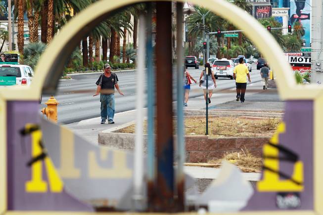 Pedestrians are seen through a broken sign at the Laughing Jackalope on the south end of the Strip Tuesday, July 15, 2014.