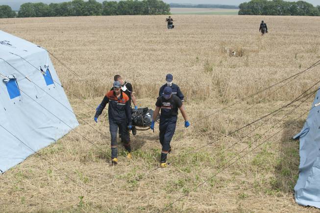 Emergency workers carry a stretcher with a victim's body in a bag at the crash site of a Malaysia Airlines jet near the village of Hrabove, eastern Ukraine, on Saturday, July 19, 2014. Ukraine accused Russia on Saturday of helping separatist rebels destroy evidence at the crash site of a Malaysia Airlines plane shot down in rebel-held territory — a charge the rebels denied.