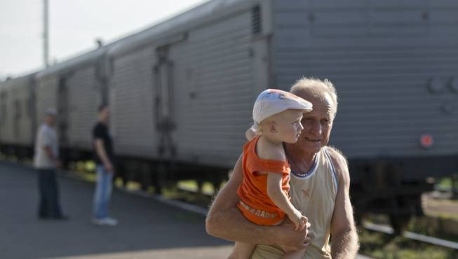 A man holds a baby as he walks next to a refrigerated train loaded with the bodies of victims, in Torez, eastern Ukraine, 15 kilometers (9 miles) from the crash site of Malaysia Airlines Flight 17, Sunday, July 20, 2014. Armed rebels forced emergency workers to hand over all 196 bodies recovered from the Malaysia Airlines crash site and had them loaded Sunday onto refrigerated train cars bound for a rebel-held city, Ukrainian officials and monitors said.