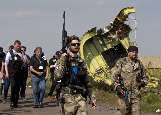Pro-Russian rebels, right, followed by members of the OSCE mission, walk by plane wreckage as they arrive for a media briefing at the crash site of Malaysia Airlines Flight 17, near the village of Hrabove, eastern Ukraine, Tuesday, July 22, 2014. A team of Malaysian investigators visited the site along with members of the OSCE mission for the first time since last week's crash.