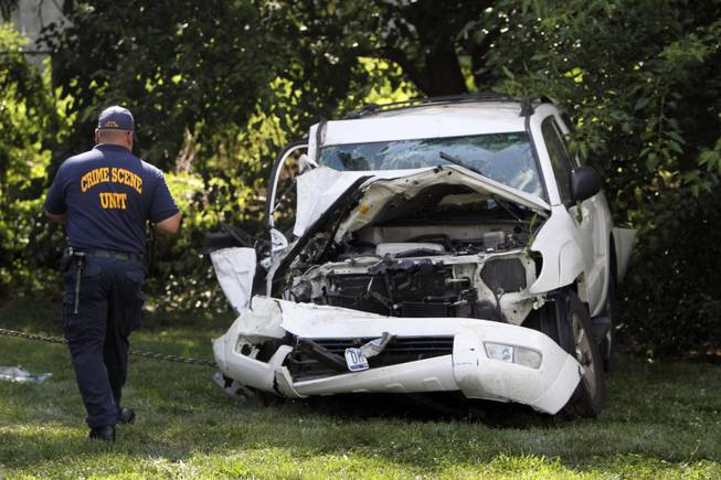 An investigator examines a heavily damaged SUV before it is towed from the scene of a fatal accident in North Philadelphia, Friday July 25, 2014.