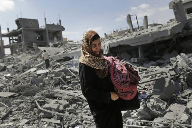 A Palestinian woman carries her belongings past the rubble of houses destroyed by Israeli strikes in Beit Hanoun, northern Gaza Strip, Saturday, July 26, 2014. Thousands of Gaza residents who had fled Israel-Hamas fighting streamed back to devastated border areas during a lull Saturday and were met by large-scale destruction: scores of homes were pulverized, wreckage blocked roads and power cables dangled in the streets. 