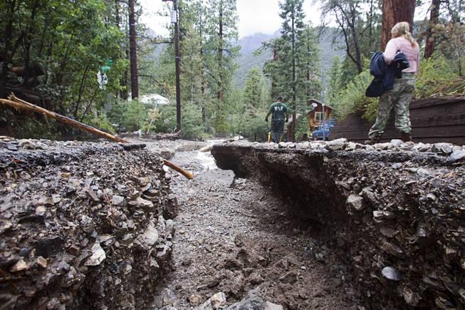 Resident Lynn Thomas, right, walks along a flood-damaged Rainbow Canyon Boulevard in the Rainbow Subdivision on Mt. Charleston Monday, July 28, 2014. The neighborhood was hit hard by flooding and debris in runoff last year as well.