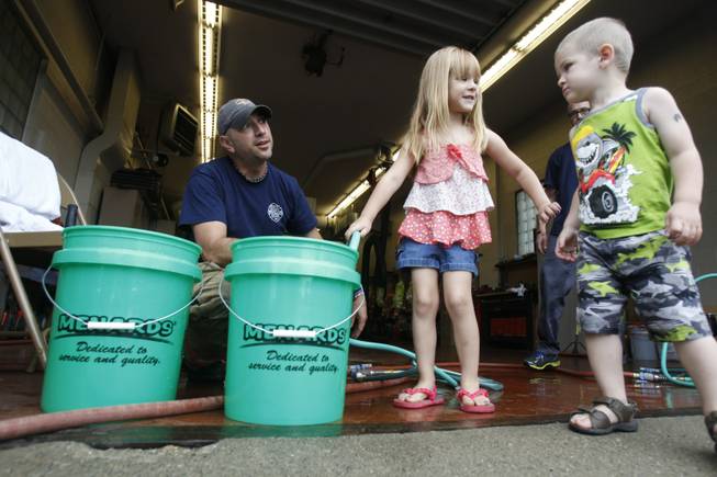 Firefighter Bryan West, left, works with Clara Cousino, 4, center, and Clay Cousino, 2, right, to fill buckets with water at the fire station in Oregon, Ohio, on Saturday, Aug. 2, 2014. Ohio's governor is declaring a state of emergency in northwest Ohio, where about 400,000 people are being warned not to drink the water.