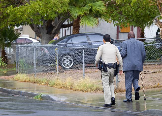 A Metro Police officer escorts a man to his home at the scene of an officer-involved-shooting near Pecos and Alexander roads August 3 , 2014.