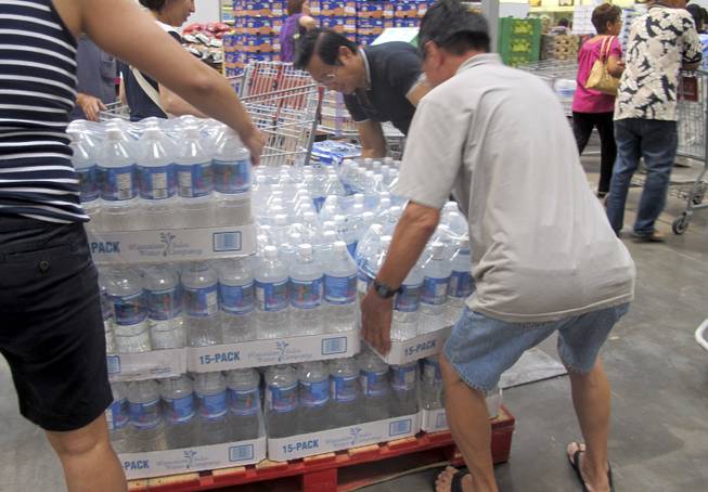 Shoppers lift cases of bottled water in preparation for a hurricane and tropical storm heading toward Hawaii at the Iwilei Costco in Honolulu on Tuesday, Aug. 5, 2014.