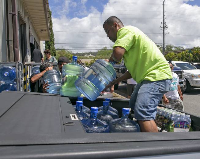 Workers at the Menehune Water Company load five gallon bottles of water into a customer's truck, Thursday, Aug. 7, 2014, in Aiea, Hawaii.  Hawaii is bracing for two back to back hurricanes, Iselle and Julio, which are on course to hit the Islands.  Bottles of water are quickly disappearing off shelves in Hawaii causing many people to line up for several hours to purchase water directly from the company.  