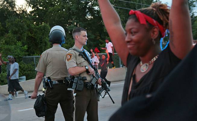 St. Louis County police officers stand back to back as they attempt to move a crowd gathered in front of the QuikTrip, Monday, Aug. 11, 2014, in Ferguson, Mo. Authorities in Ferguson used tear gas and rubber bullets to try to disperse a large crowd Monday night that had gathered at the site of a burned-out convenience store damaged a night earlier, when many businesses in the area were looted.