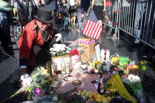 Gregg Donovan places flowers on the star of actor-comedian Robin Williams at a makeshift memorial along the Hollywood Walk of Fame in Los Angeles on Tuesday, Aug. 12, 2014. Williams, 63, died at his San Francisco Bay Area home Monday in an apparent suicide. (AP Photo/Nick Ut)