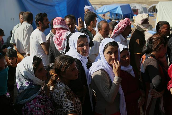 Displaced Iraqis from the Yazidi community gather for humanitarian aid at Nowruz camp, in Derike, Syria, Tuesday, Aug. 12, 2014. In the camps here, Iraqi refugees have new heroes: Syrian Kurdish fighters who battled militants to carve an escape route to tens of thousands trapped on a mountaintop. 