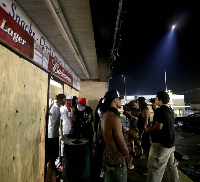 People stand in front of a convenience store after it was looted early Saturday, Aug. 16, 2014, in Ferguson, Mo. The violence stemmed from the shooting death of Michael Brown by police a week ago after the teen allegedly stole  a box of cigars from the store.