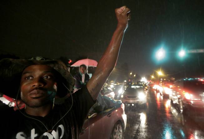 A protester holds up a clenched fist Friday, Aug. 15, 2014, in front of a convenience store that was looted and burned following the shooting death of Michael Brown by police nearly a week ago in Ferguson, Mo.  A suburban St. Louis police chief on Friday identified the officer whose fatal shooting ignited days of heated protests, and released documents alleging the teen was killed after a robbery in which he was suspected of stealing a box of cigars.