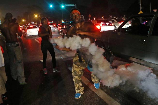 A protester tries to throw tear gas back at the police in Ferguson, Mo., Sunday, Aug. 17, 2014. Protests over the killing of 18-year-old Michael Brown by a white police officer have entered their second week. 