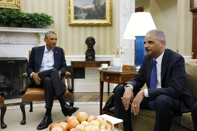 President Barack Obama speaks with Attorney General Eric Holder as news photographers photograph their meeting regarding the fatal police shooting of a black teenager in Ferguson, Missouri, Monday, Aug. 18, 2014, in the Oval Office of the White House in Washington.