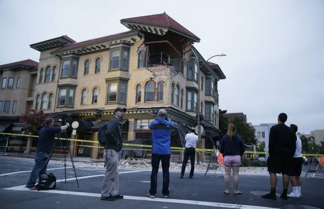 People look at a damaged building with a top corner exposed following an earthquake Sunday, Aug. 24, 2014, in Napa, Calif. A large earthquake rolled through California's northern Bay Area early Sunday, damaging some buildings, igniting fires, knocking out power to tens of thousands and sending residents running out of their homes in the darkness.