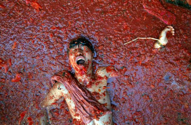 AP10ThingsToSee- A man lies in a puddle of squashed tomatoes, during the annual "tomatina" tomato fight fiesta in the village of Bunol, 50 kilometers outside Valencia, Spain, Wednesday, Aug. 27, 2014. (AP Photo/Alberto Saiz)