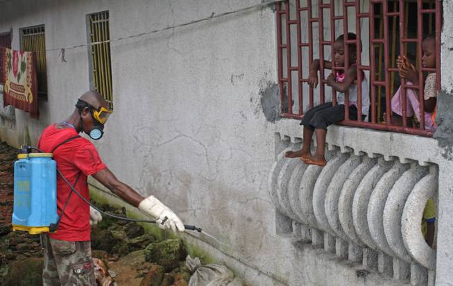 A man that was hired by the community sprays chemicals to try and prevent the spread of the Ebola virus, as local children look on, in Monrovia, Liberia, Friday, Aug. 29, 2014. The Ebola outbreak in West Africa eventually could exceed 20,000 cases, more than six times as many as are now known, the World Health Organization said Thursday. A new plan released by the U.N. health agency to stop Ebola also assumes that the actual number of cases in many hard-hit areas may be two to four times higher than currently reported.