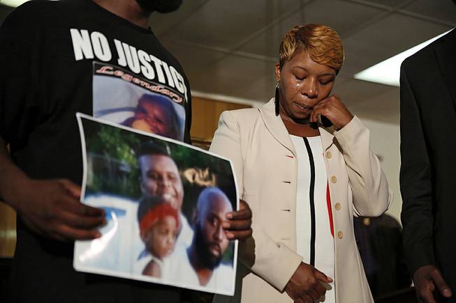 In this Aug. 11, 2014 file photo, Lesley McSpadden, the mother of 18-year-old Michael Brown, wipes away tears as Brown's father, Michael Brown Sr., holds up a family picture of himself, his son, top left, and a young child during a news conference in Jennings, Mo. Lingering questions about Michael Brown could be answered Wednesday as two news organizations seek the release of any possible juvenile records for the unarmed 18-year-old who was shot by a police officer last month.


