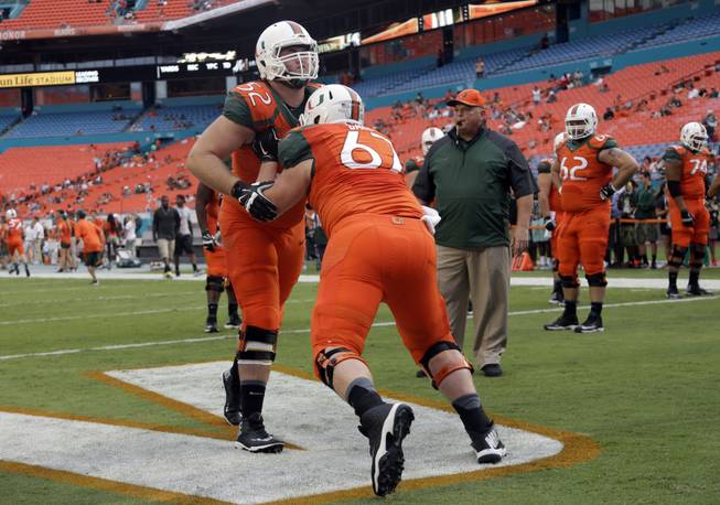 Miami linebacker Denzel Perryman (52) and offensive linesman Alex Gall do drills before an NCAA football game, against Florida A&M Saturday, Sept. 6, 2014, in Miami Gardens, Fla. At right is offensive line coach Art Kehoe. (AP Photo/Lynne Sladky)