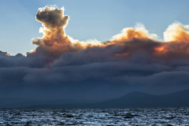 This Wednesday, Sept. 17, 2014 photo shows smoke from a California wildfire rising behind Lake Tahoe as seen from the Nevada side of the lake near Incline Village, Nev. Higher humidity Friday helped slow the growth of the massive Northern California wildfire that authorities say was set deliberately and has forced some 2,800 people to evacuate. 