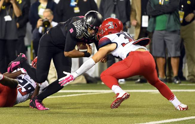 Oregon quarterback Marcus Mariota (8) runs for a touchdown as Arizona safety Jared Tevis (38) closes in during the second quarter of an NCAA college football game Thursday, Oct. 2, 2014, in Eugene, Ore. (AP Photo/Steve Dykes)