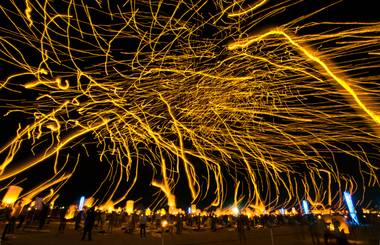 Lanterns float into the night sky on a long exposure leaving light trails as more are inflated for release during the Rise Lantern Festival at Jean Dry Lake Bed on Saturday, Oct. 18, 2014, in Jean.