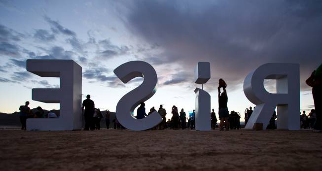 Participants pose for pictures on the giant letters at the Rise Lantern Festival at Jean Dry Lake Bed as the sun sets Saturday, Oct. 18, 2014.