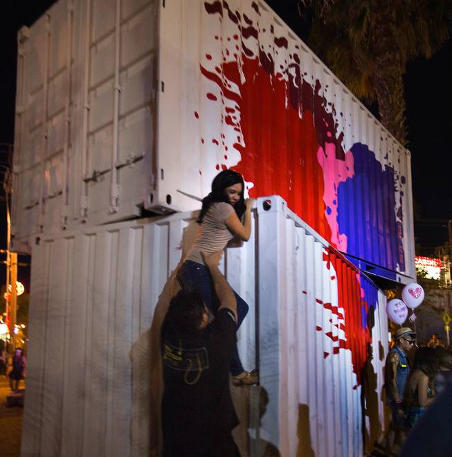 An attendee is helped down from atop painted containers during opening day of the Life is Beautiful Festival on Friday, October 24, 2014.