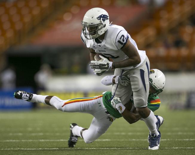 Nevada wide receiver Hasaan Henderson (12) gets pulled down by Hawaii defensive back Dee Maggitt (23) in the second quarter of the NCAA college football game, Saturday, Oct. 25, 2014, in Honolulu. (AP Photo/Marco Garcia)