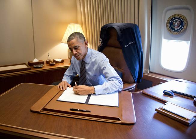 President Barack Obama signs two presidential memoranda associated with his actions on immigration in his office, on Air Force One as he arrives at McCarran International Airport in Las Vegas, Friday, Nov. 21, 2014.