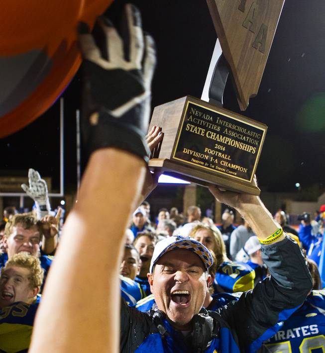 Moapa Valley's head coach Brent Lewis is doused with iced water while holding the winning trophy after the Division I-A state high school football championship game on Saturday, November 22, 2014.